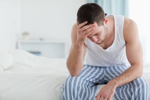 Ill man sitting on his bed with his head on his hand-1