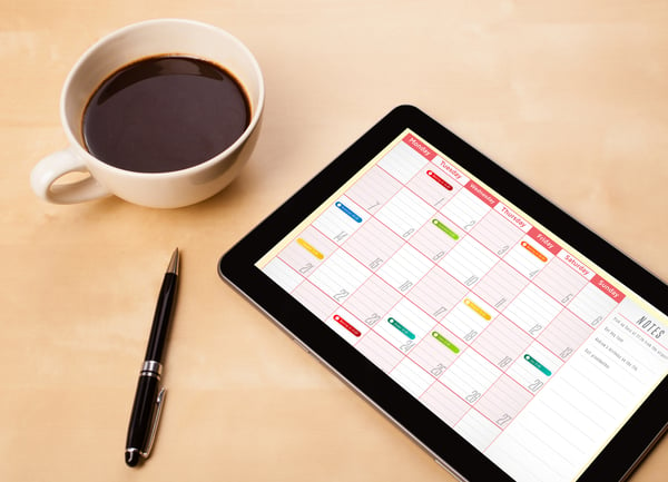 Workplace with tablet pc showing calendar and a cup of coffee on a wooden work table close-up