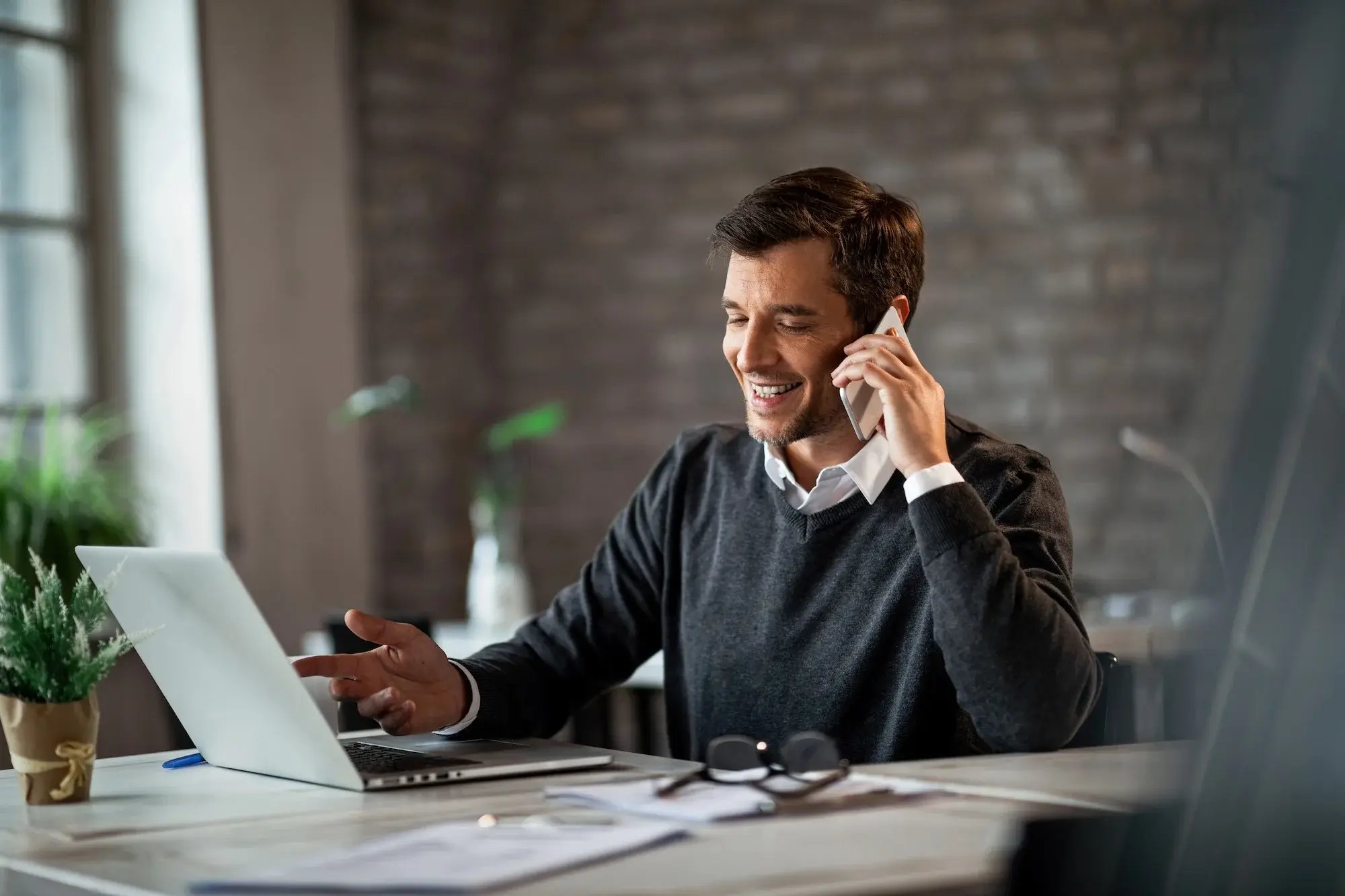 A man on the phone with an open laptop at his desk.